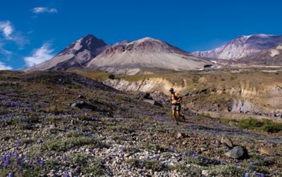 Yassine Diboun runs across a beautiful landscape with purple wildflowers in the foreground and mountains in the background.