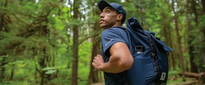 A hiker pauses in a lush green forest to look at the scenery.  
