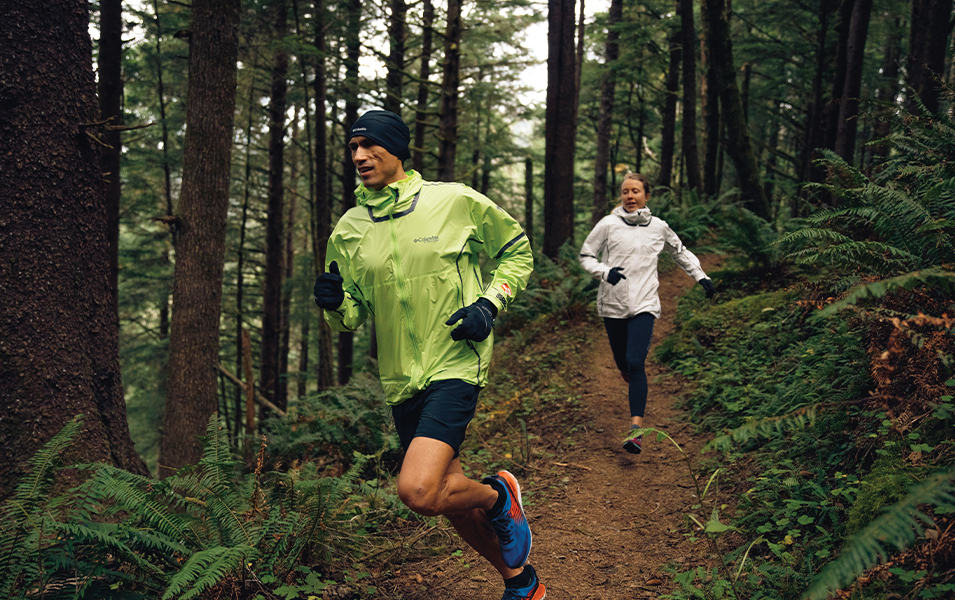 Man and a woman running on a forest trail. 