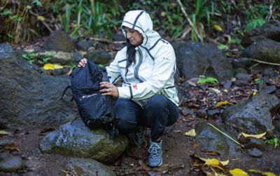 Woman holding a backpack sitting on a rock in the woods. 