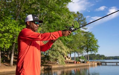 Mark Daniels Jr. casting his line into the water while wearing Performance Fishing Gear on a sunny day along a shoreline.