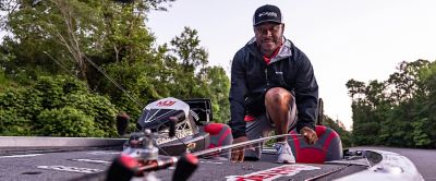 Mark Daniels Jr. crouching down on the deck of a boat to pick up his rod while wearing Performance Fishing gear.