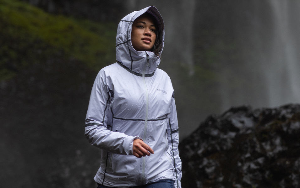 A woman wearing a lavender colored Columbia Sportswear OutDry™ Extreme rain jacket hikes through a misty scenic area.