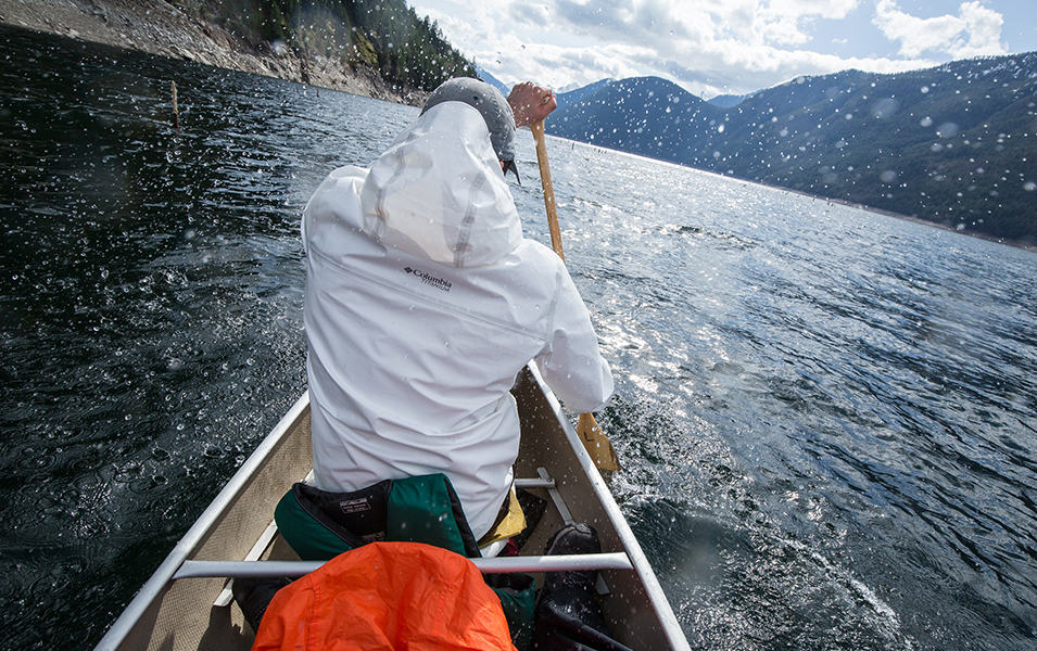 A man wearing a white Columbia Sportswear OutDry™ Extreme jacket paddles away from the camera in a canoe. 