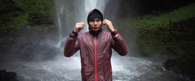 A man wearing a red Columbia Sportswear OutDry™ Extreme rain jacket stands in front of a waterfall staring at the camera. 