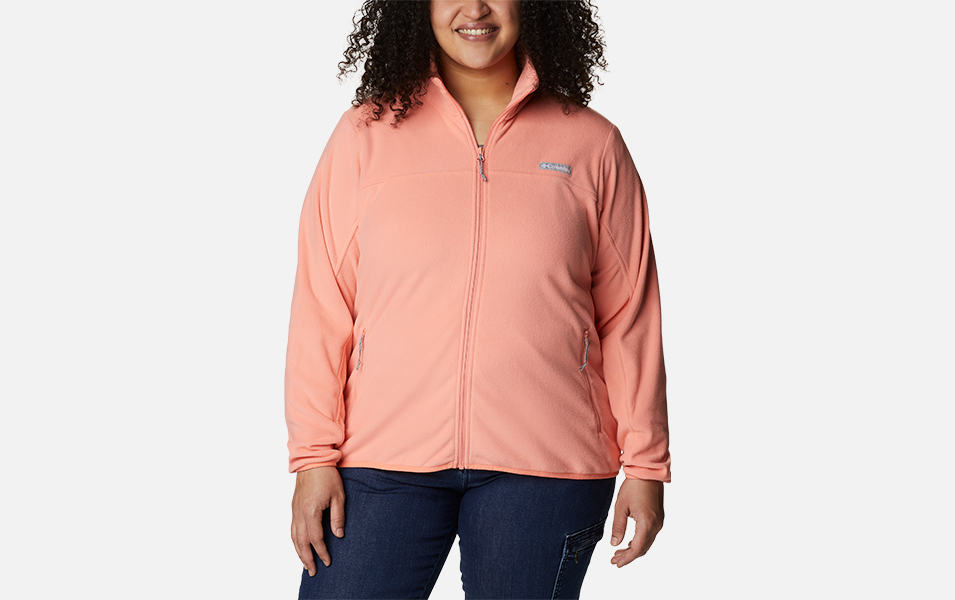 A woman models a light orange Columbia Sportswear Ali Peak full zip fleece jacket with a white background.