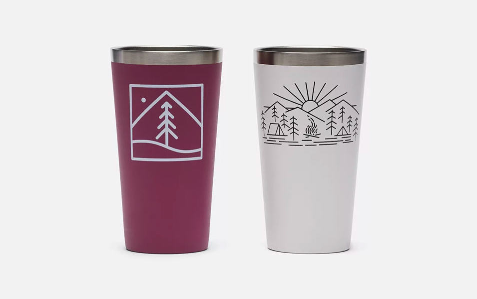 A product image of two Columbia Sportswear double wall vacuum pint cups set against a white background. One pint cup is purple with a tree sketch on it and the other is white with the sketch of a campground scene. 
