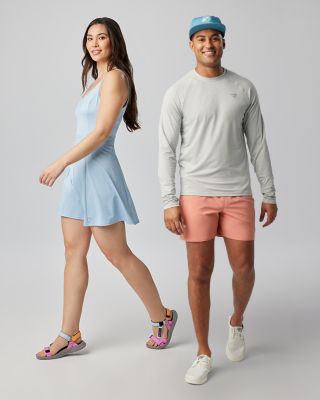 A man and a woman posing in a studio setting in cool outdoor outfits.