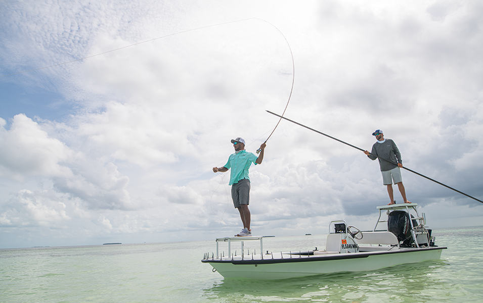 Two men fish from a boat in a sunny location.
