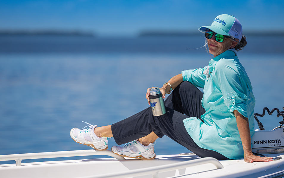 A woman in a UPF fishing shirt sits on a boat on a beautiful sunny day. 