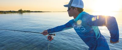 A fisherman wearing a UPF-rated shirt casts his rod into the blue ocean with the sunset in the background. 
