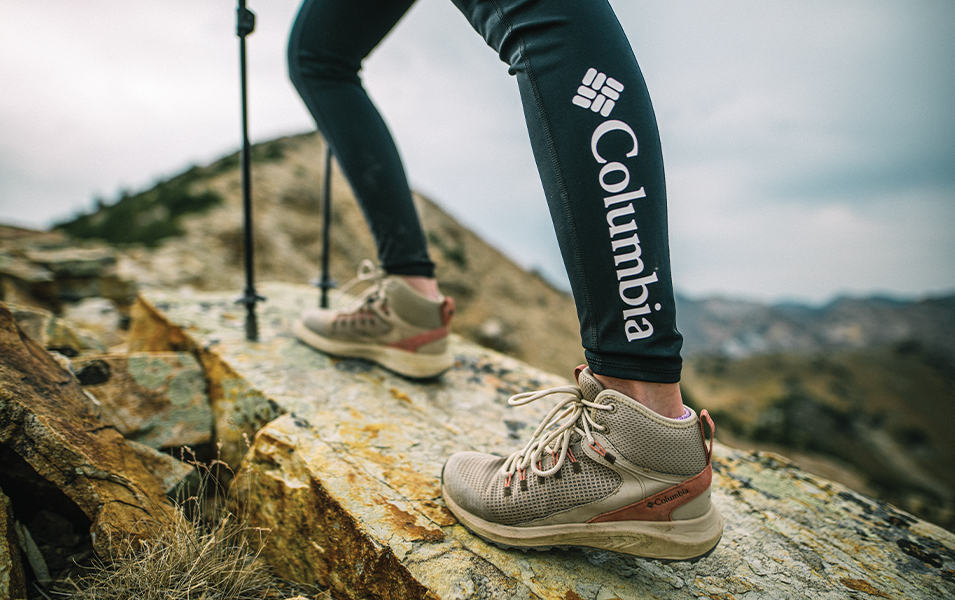 A woman's legs are pictured in black Columbia Sportswear leggings with a set of trekking poles in the background.