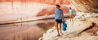 Woman and man walking along river bank in rocky canyon. 