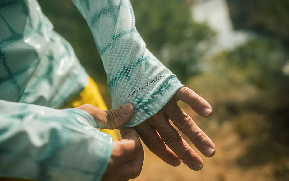 A close-up shot of a trail runner’s hand tugging at the sleeve of a Columbia Sportswear UPF-rated shirt featuring Omni-Shade™ fabric.