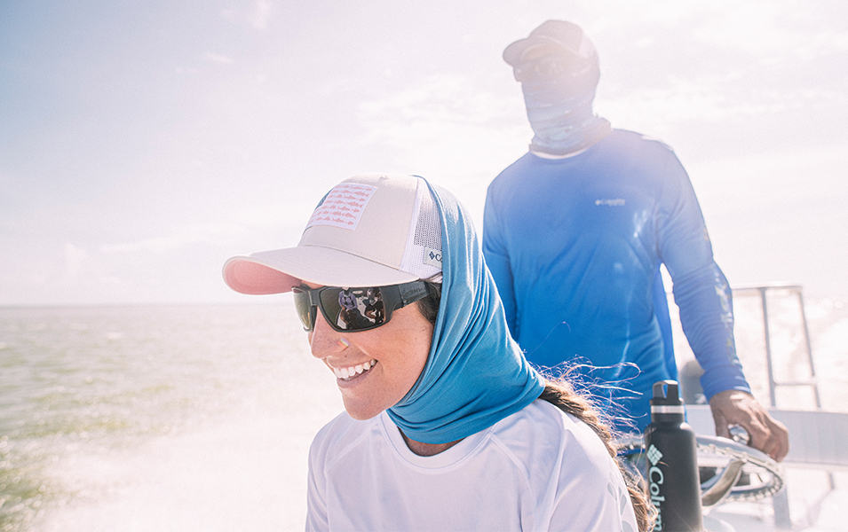 A woman wearing a blue Columbia Sportswear neck gaiter smiles on a boat as a man in a blue shirt stands behind her. 