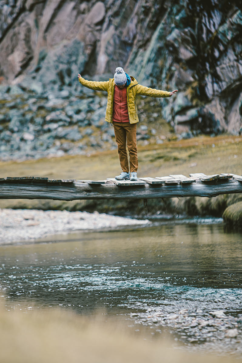 Charlotte on a rickety old bridge in Peru, layered up in her Super DS Jacket.