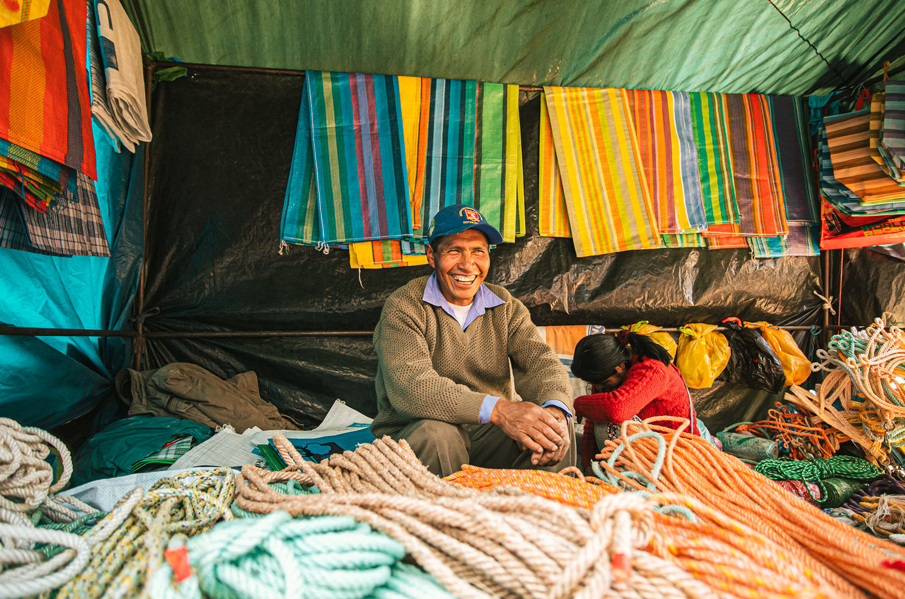 At the farmers market in the center square of Pitumarca, Peru, a man sits in his booth with all kinds of rope and material for sale.
