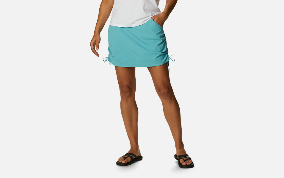 A product shot of a woman wearing a light blue Columbia Sportswear Anytime Casual skort with a gray background.