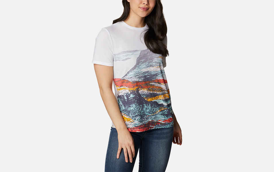 A product shot of a woman wearing a colorful Columbia Sportswear Daisy Days t-shirt and jeans with a gray background.