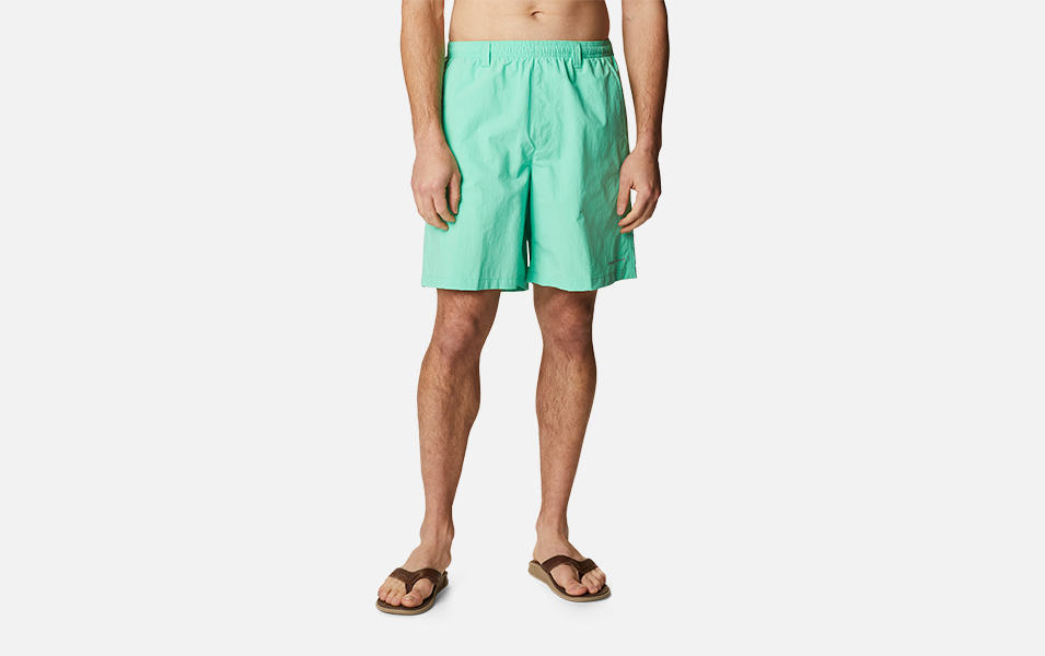 A product shot of a man wearing turquoise Columbia Sportswear PFG Backcast II water shorts with a gray background.