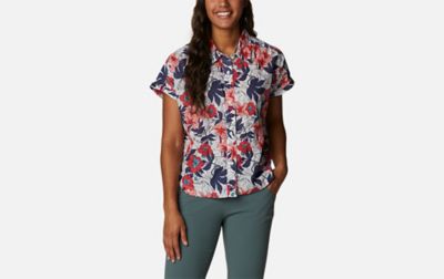 A product shot of a woman wearing a pink-and-purple floral Columbia Sportswear Camp Henry IV button-down shirt and blue pants with a gray background.