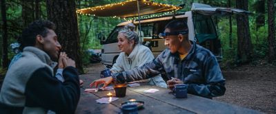 A group of friends playing cards at a campsite picnic table.