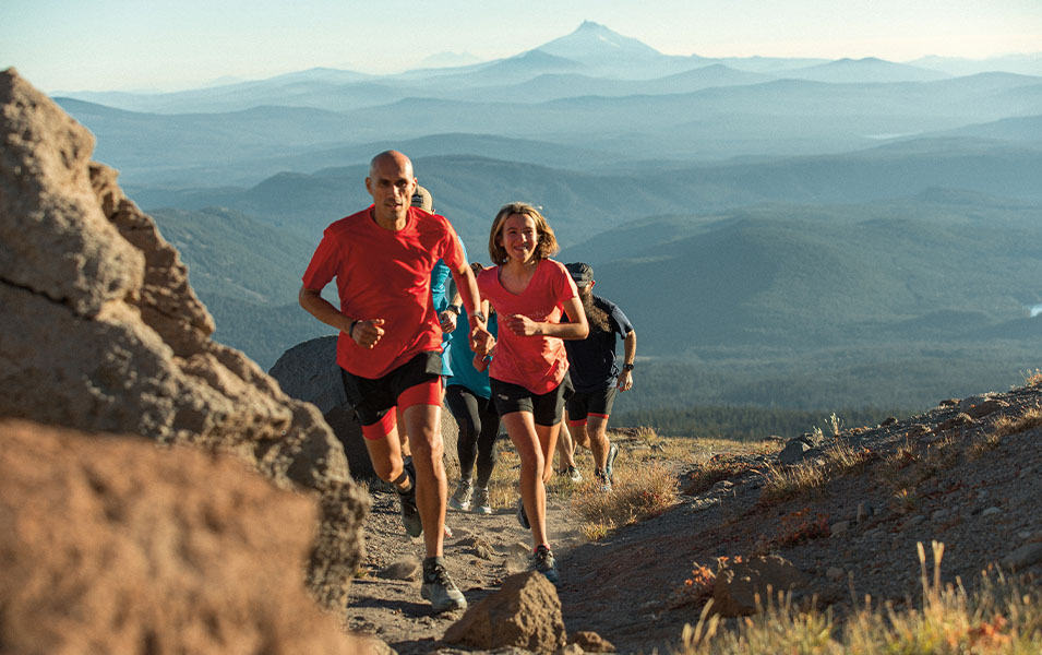 A group of tail runners comes up a mountain trail with gorgeous peaks in the background.  