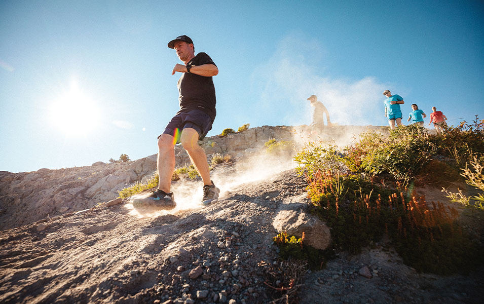 A trail runner comes down a rocky hill as other athletes trail behind him. 