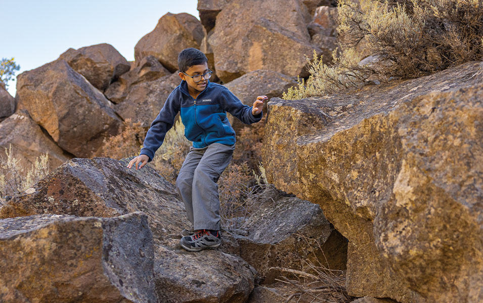 Un garçon souriant descend un sentier de randonnée à travers de gros rochers.