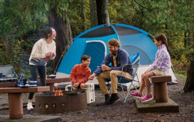 A family gathers around a fire tent with their tent pitched behind them.