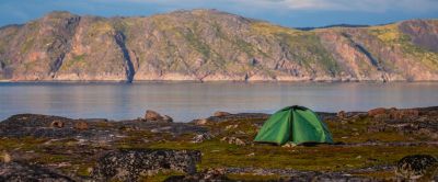 A lone green tent is pitched on a flat, grassy area, a safe distance from the lake's shoreline.