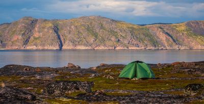 A lone green tent is pitched on a flat, grassy area, a safe distance from the lake's shoreline.