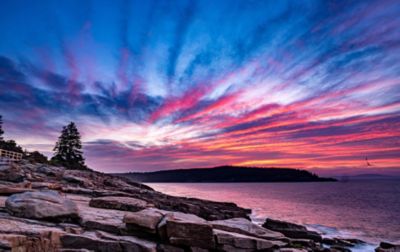 A dramatic blue, purple and rose sunset illuminates big flat rocks extending to the shoreline in Acadia National Park. 