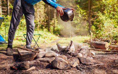  A camper expertly douses a campfire with a large kettle of water.