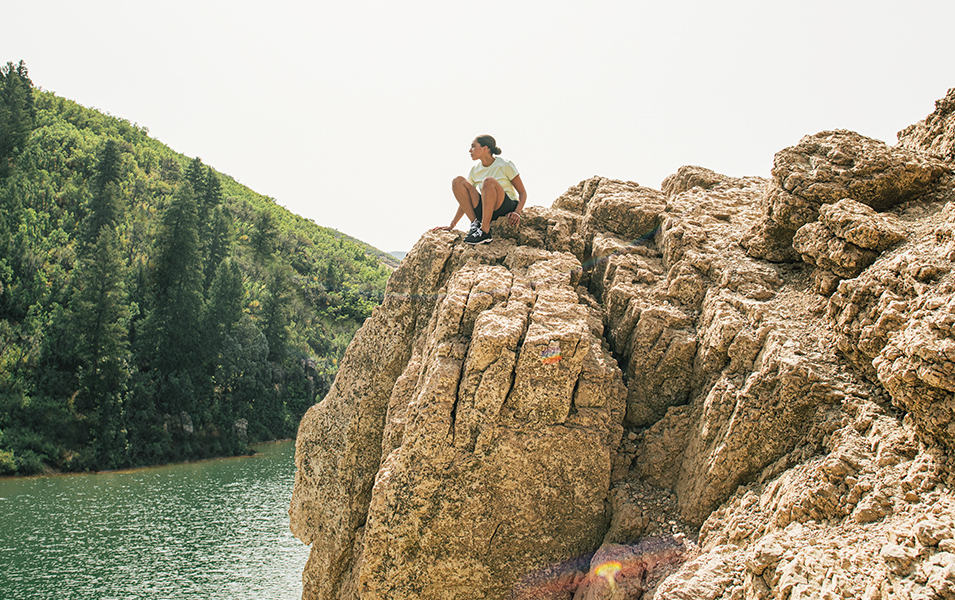 Woman sitting on rock outcropping over lake. 