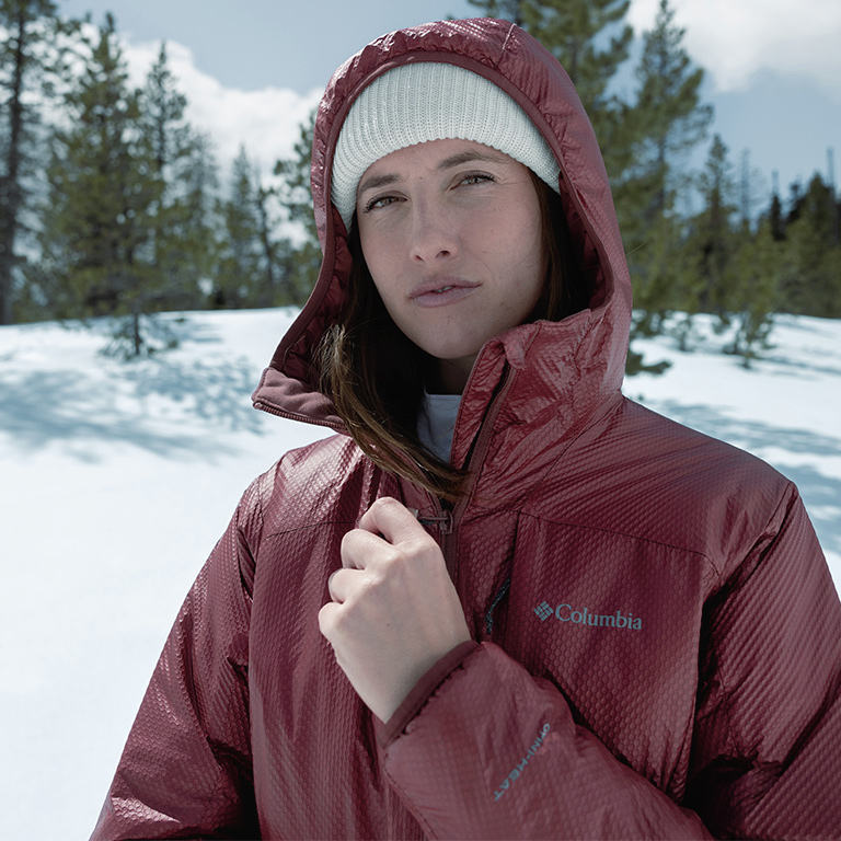 A man in a red Arch Rock Double Wall Elite insulated jacket hiking in a snowy forest.