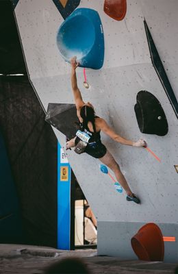 Kyra Condie in middle of a bouldering competition, holds on to the wall, thinking about next placement