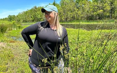 Chelsea McCurdy stands amid green foliage in Allsopp Park, Arkansas, wearing Columbia Sportswear’s Leslie Falls long sleeve hiking top. 