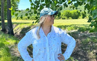 Chelsea McCurdy stands in a sunny field with trees all around her wearing Columbia Sportwear’s Silver Ridge Utility shirt. 