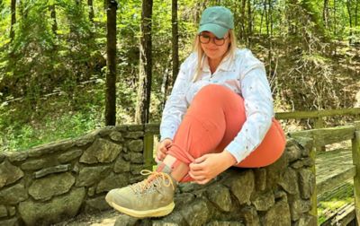 Chelsea McCurdy sits on a pretty stone wall on a hiking trail at Cadron Settlement Park, rolling up the leg of Columbia Sportswear’s Saturday Trail™ Stretch Pants.