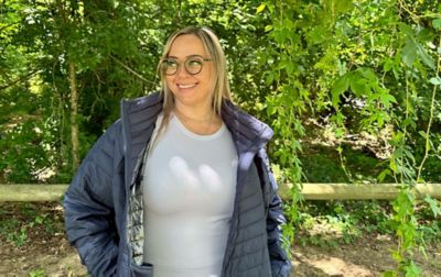 Chelsea McCurdy stands in a scenic outdoor setting at Toad Suck State Park wearing a blue-gray Powder Lite hiking jacket. 