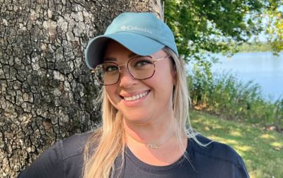Chelsea McCurdy smiles widely for the camera at Yellowstone National Park wearing a Columbia Sportwear Coolhead II ball cap with a beautiful lake behind her. 