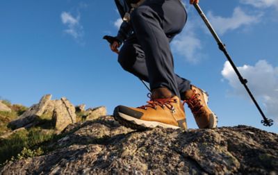 Jambes d'un randonneur portant des bottes de randonnée Columbia Sportswear marchant sur une colline rocheuse.