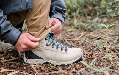 Une personne ajuste son pantalon pour le porter sur une chaussure de randonnée Columbia.
