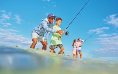 Two children have fun learning to fish with their parents. They are outfitted for a day of saltwater fishing in sun-protective apparel.