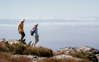 Two hikers are making their way along a grassy ridge above an ocean. 