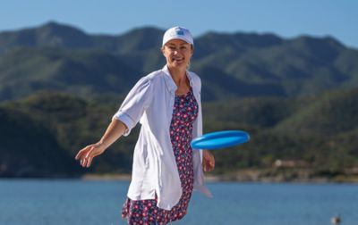 A woman with hills and a lake in the background, tosses a frisbee.