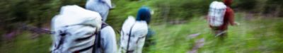Abstract motion blur image of hikers crossing a stream, wearing large backpacks and outdoor gear. The photo captures dynamic movement with streaks of color, emphasizing speed, activity, and the energy of backcountry adventure.