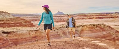 High on a desert plateau, two hikers wearing caps and sun-protective apparel enjoy expansive views. 