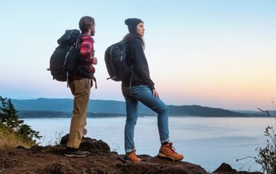 Two hikers stand on a trail overlooking a beautiful body of water at dusk. 